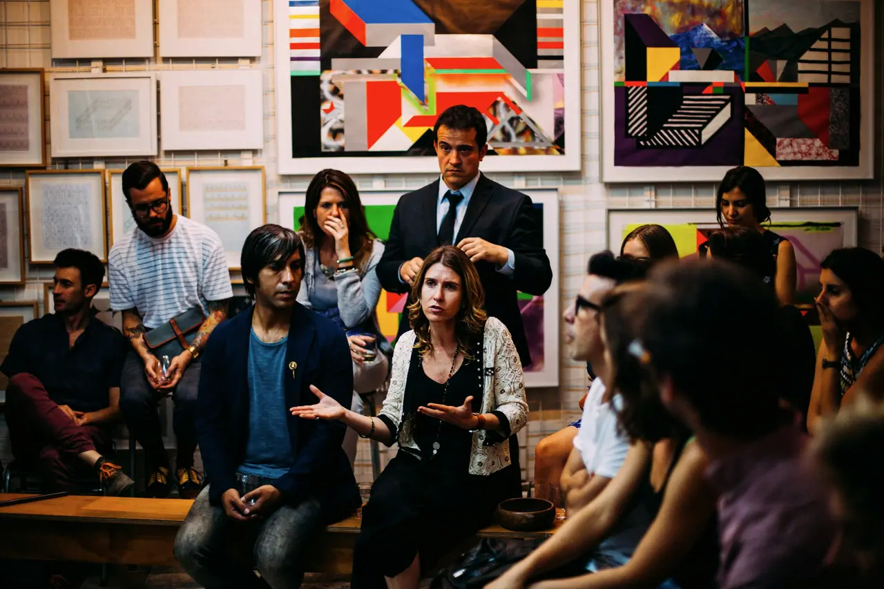 A group in a gallery space listening as one woman speaks, others leaning in