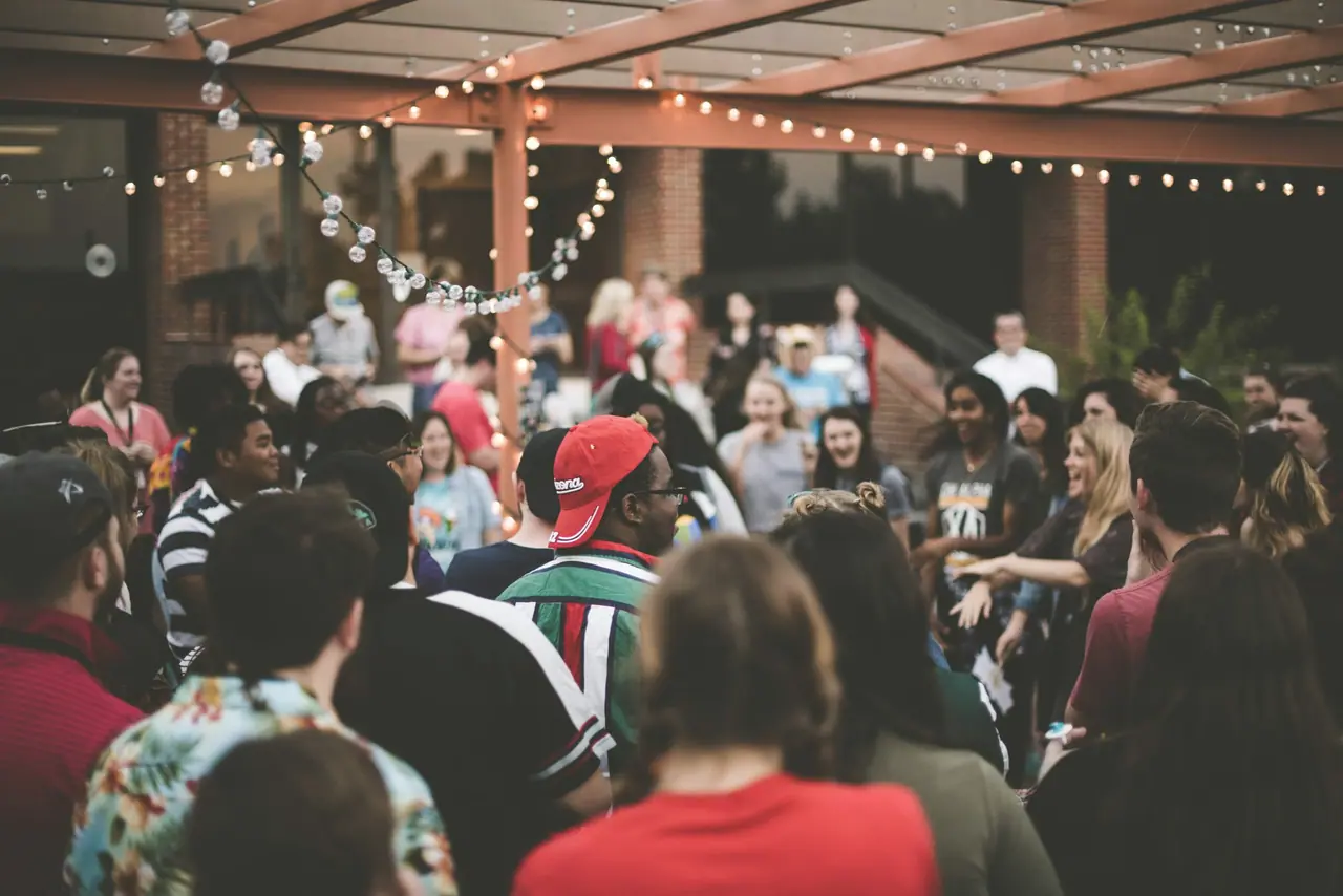 A crowd at an evening event in a courtyard strung with lights